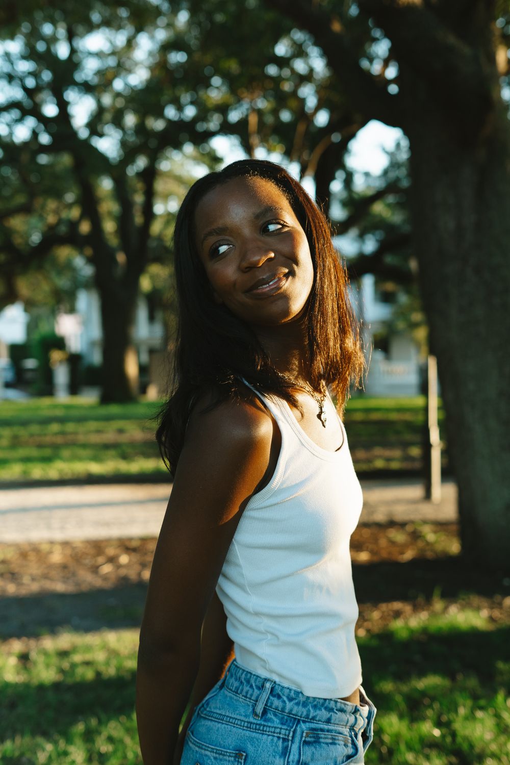 Outdoor portrait in a park setting with white tank top and denim during golden hour lighting.