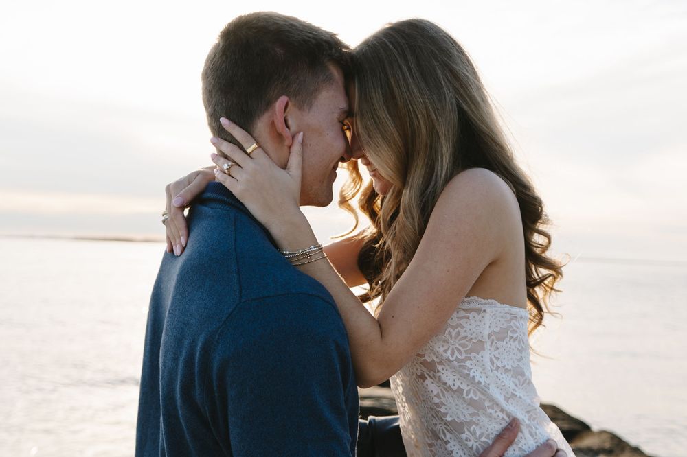 Romantic couple shares intimate moments during sunset beach photo session in coordinating navy and white outfits.