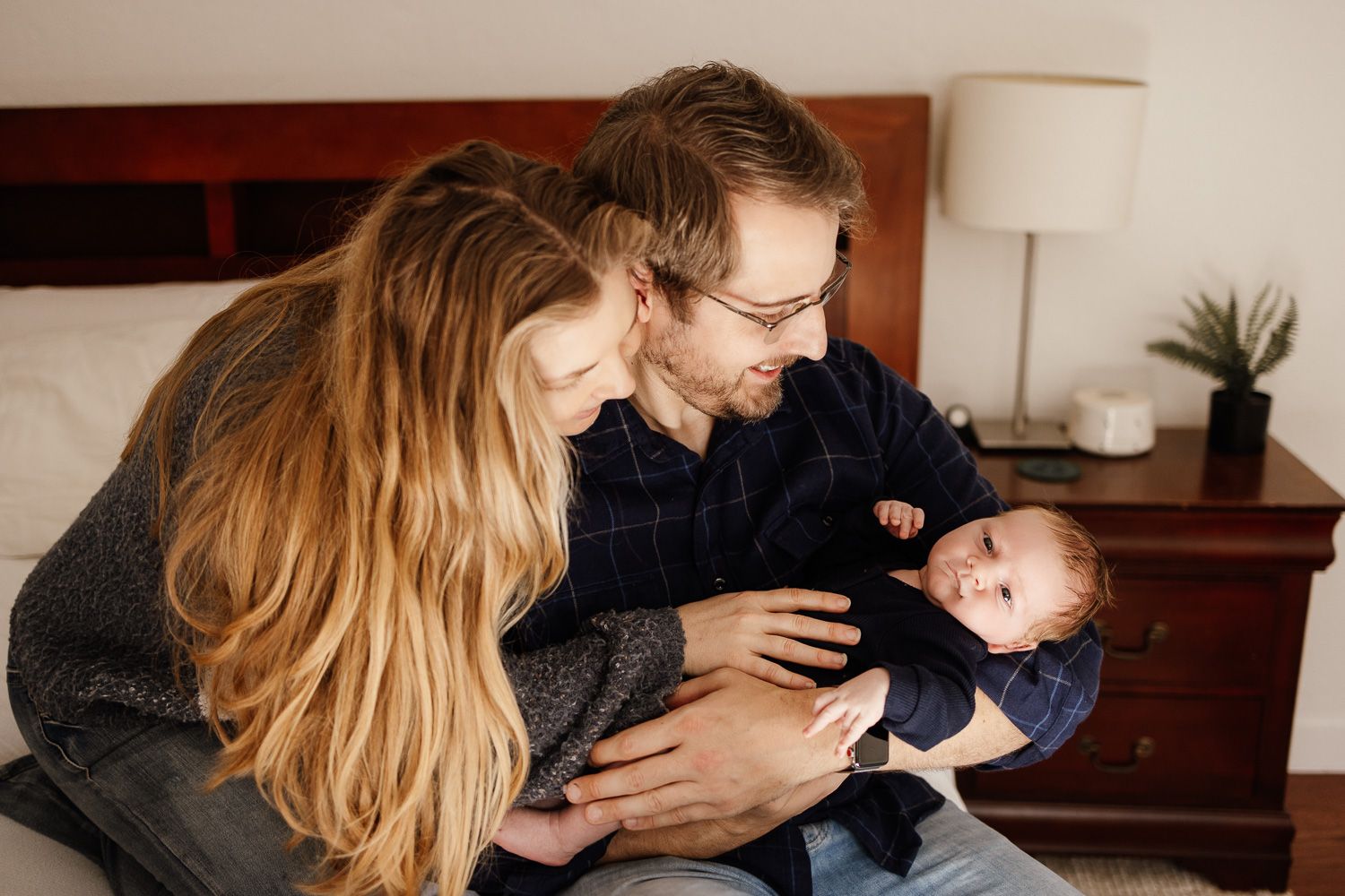 A mom and dad cuddle their new baby at their in-home lifestyle newborn photoshoot in San Jose