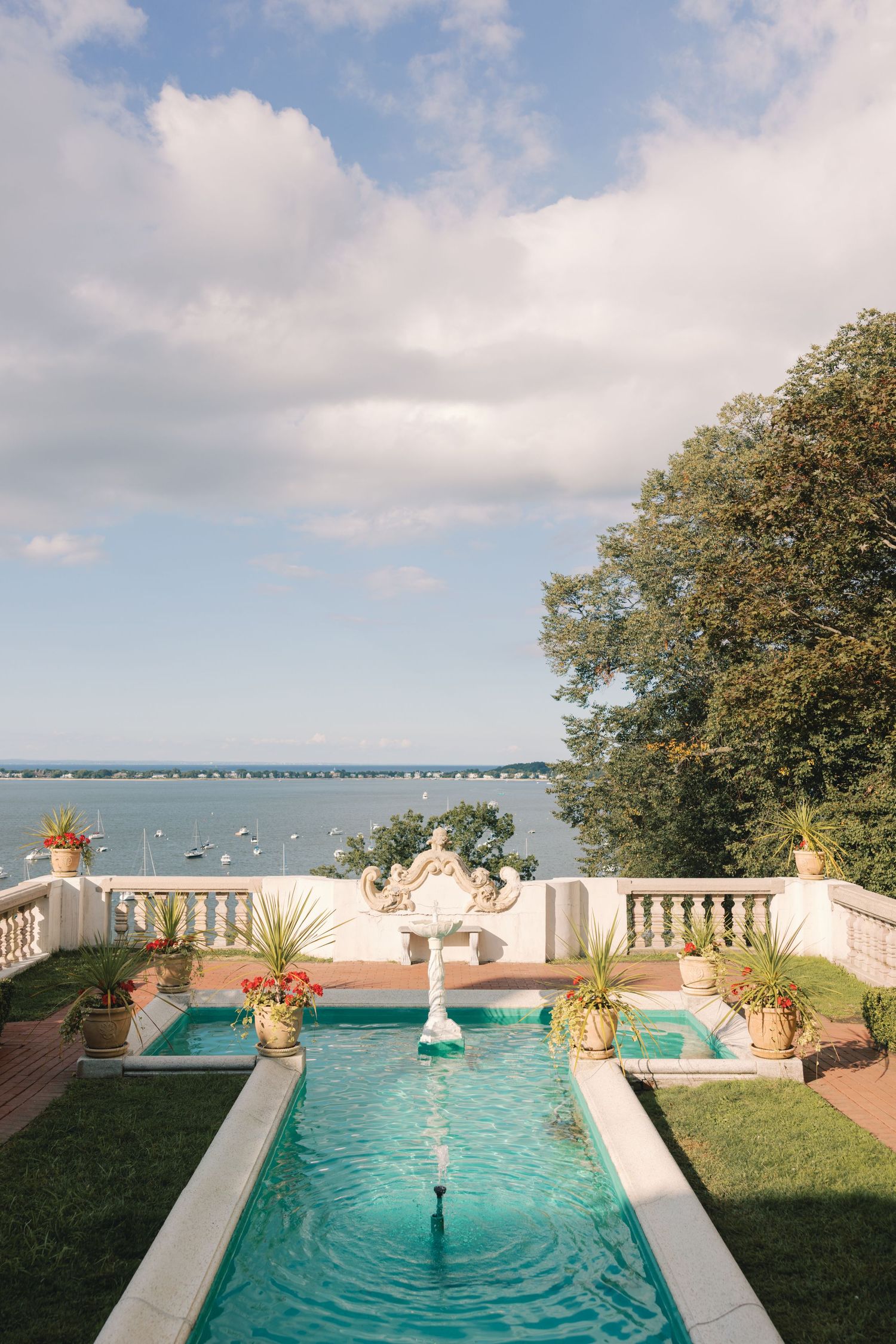 Elegant estate terrace with fountain pool overlooking scenic waterfront and sailboats.