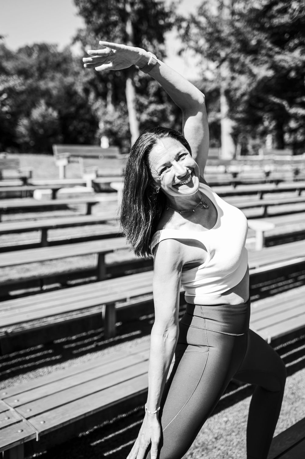 Black and white photo of person doing yoga stretches on wooden bleachers in a park setting.