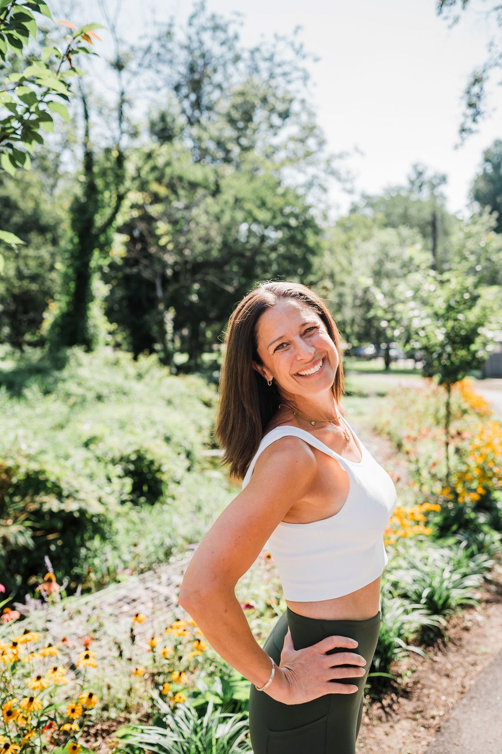 A woman in a green and white outfit enjoys a sunny day in a garden path surrounded by blooming yellow flowers.