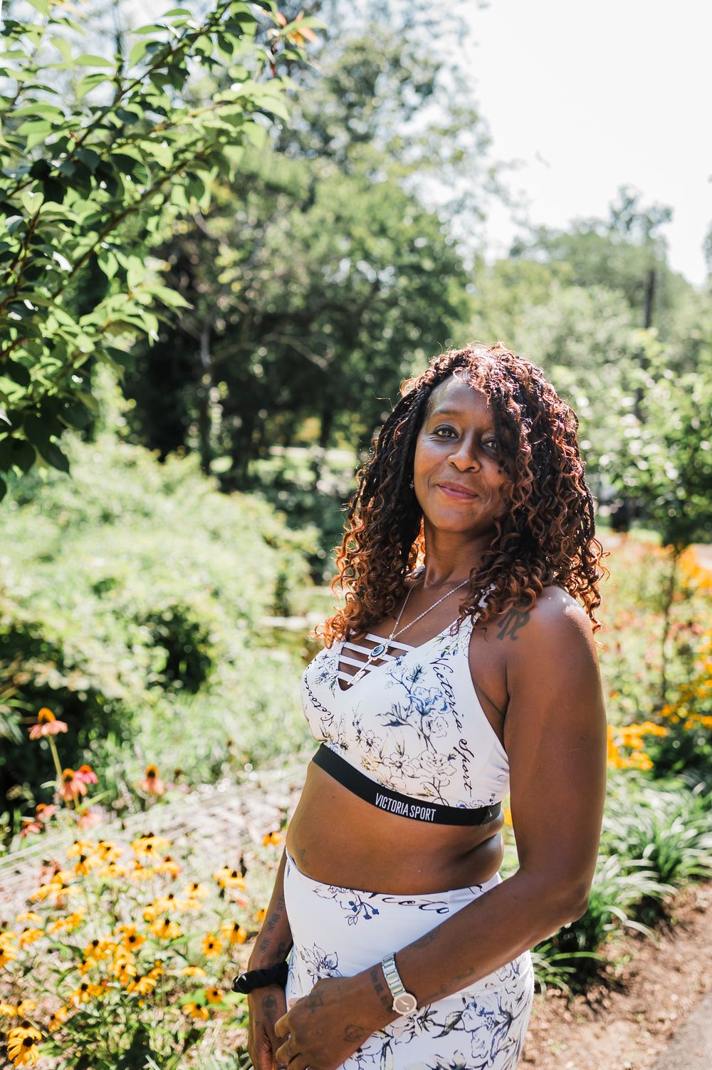 A candid fashion photoshoot in a lush garden setting with vibrant orange flowers blooming in the background.