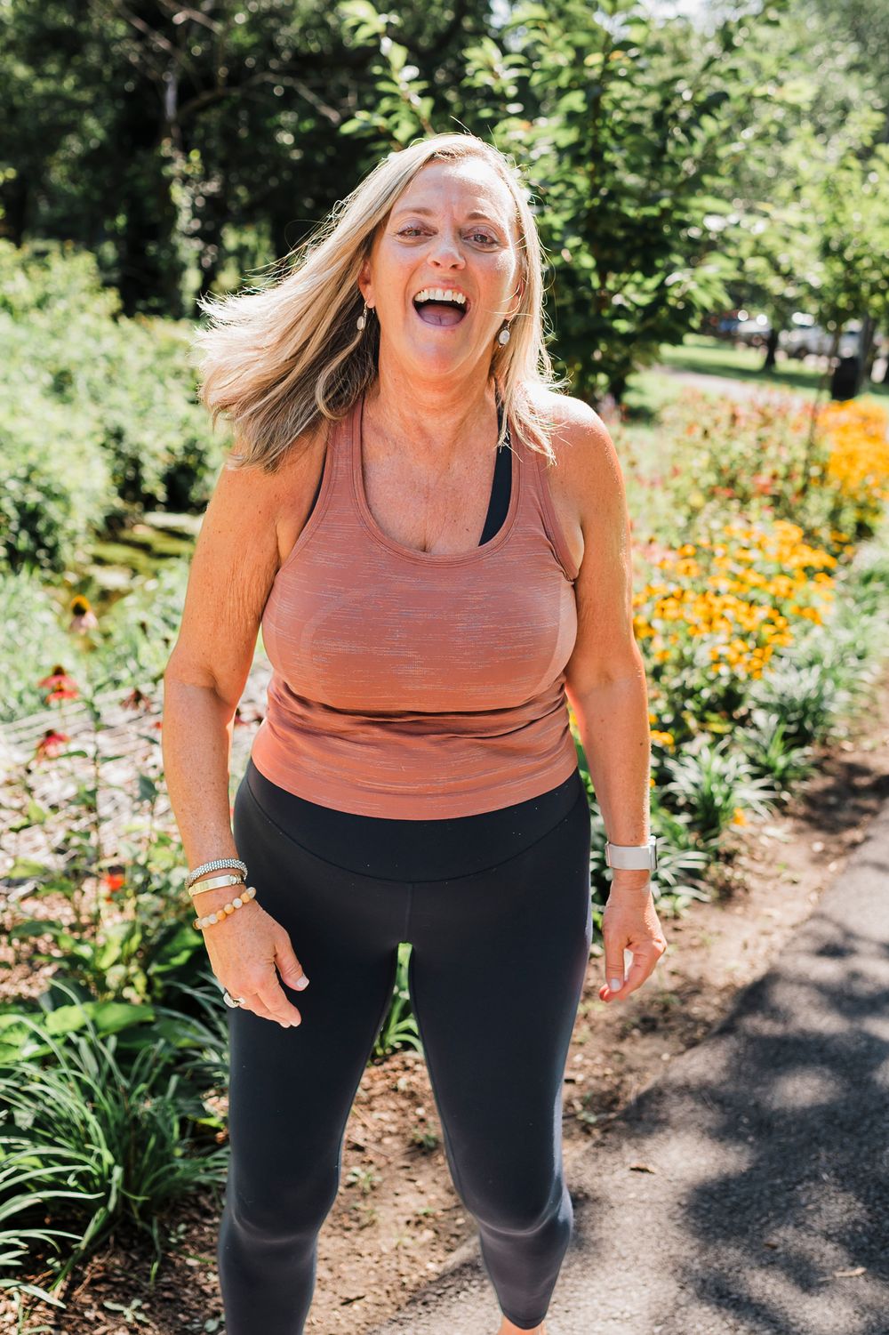 Person exercising outdoors with black leggings and coral tank top in front of colorful flower garden setting.