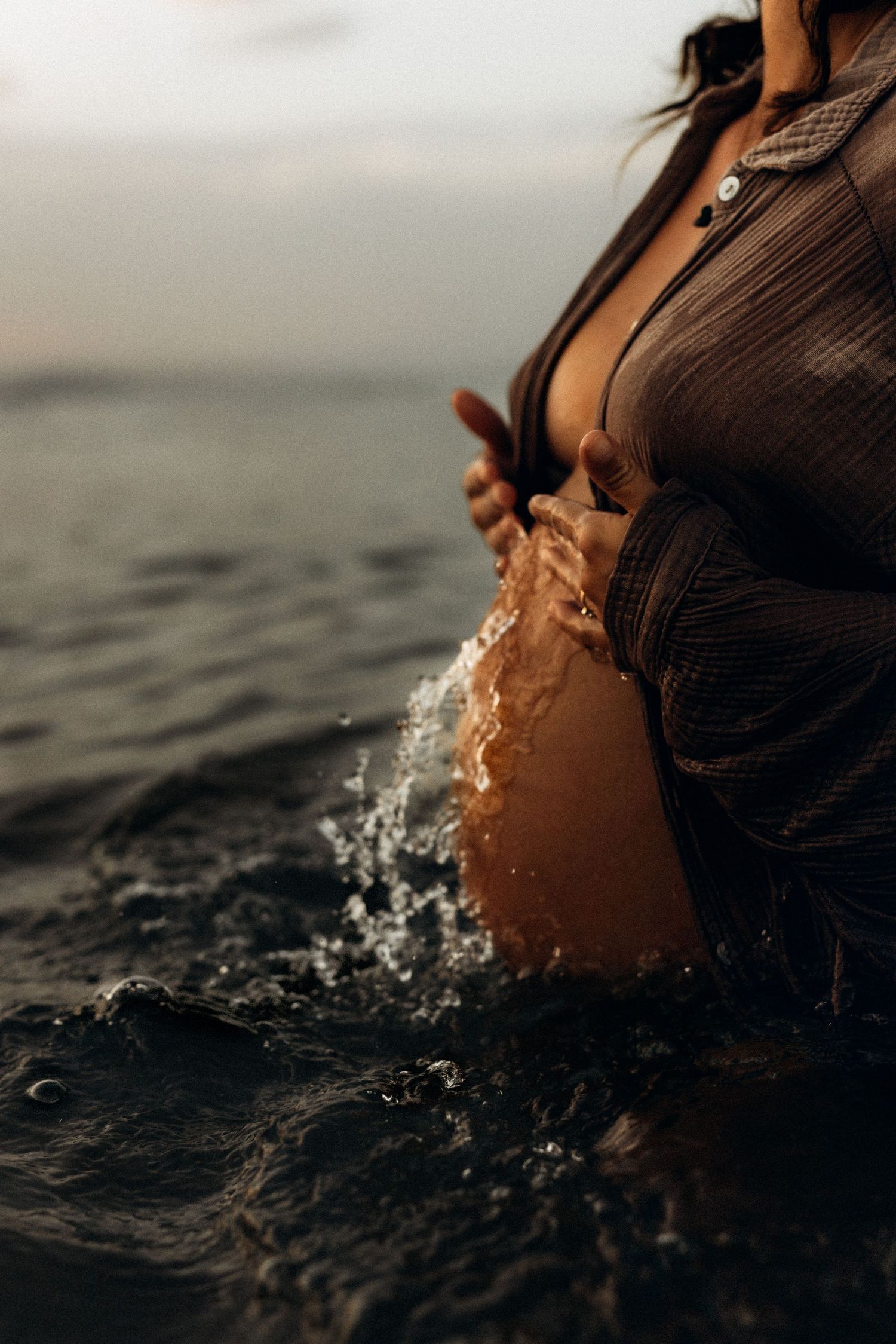 Artistic close-up of a person wearing a brown blouse standing in dark water with splashing droplets at sunset with a photographer Denia