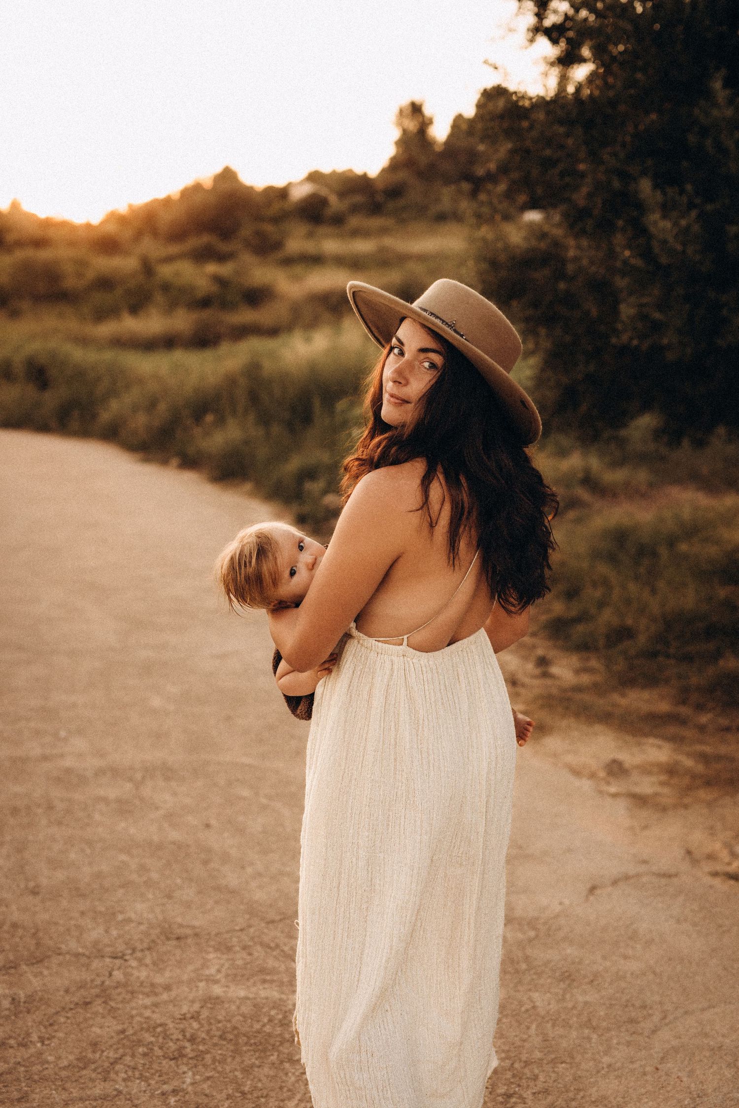Woman in flowy white dress and sun hat dances joyfully on a dirt path during golden hour. Javea photographer