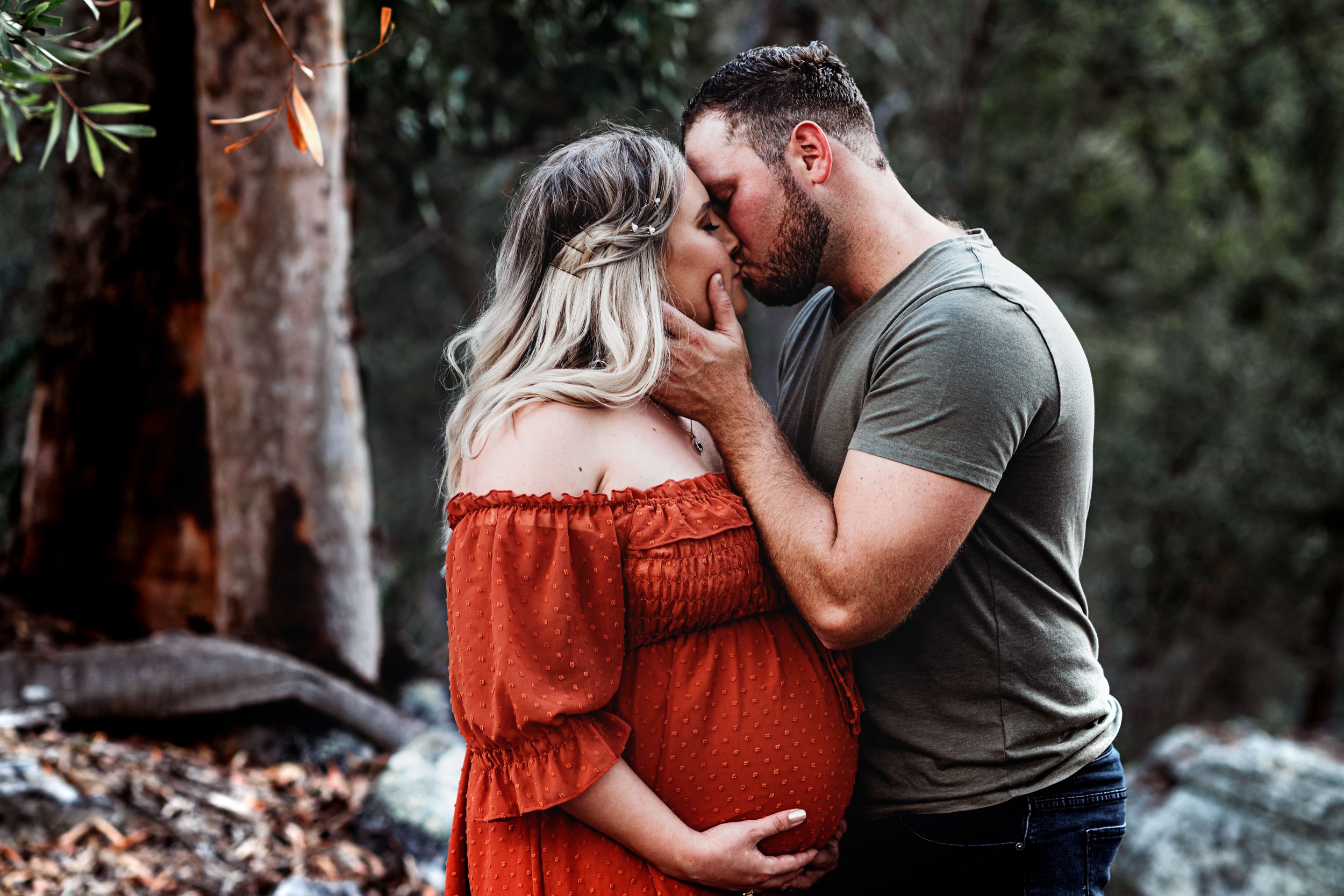 A romantic maternity photo featuring an intimate moment between a couple outdoors against a natural forest backdrop.
