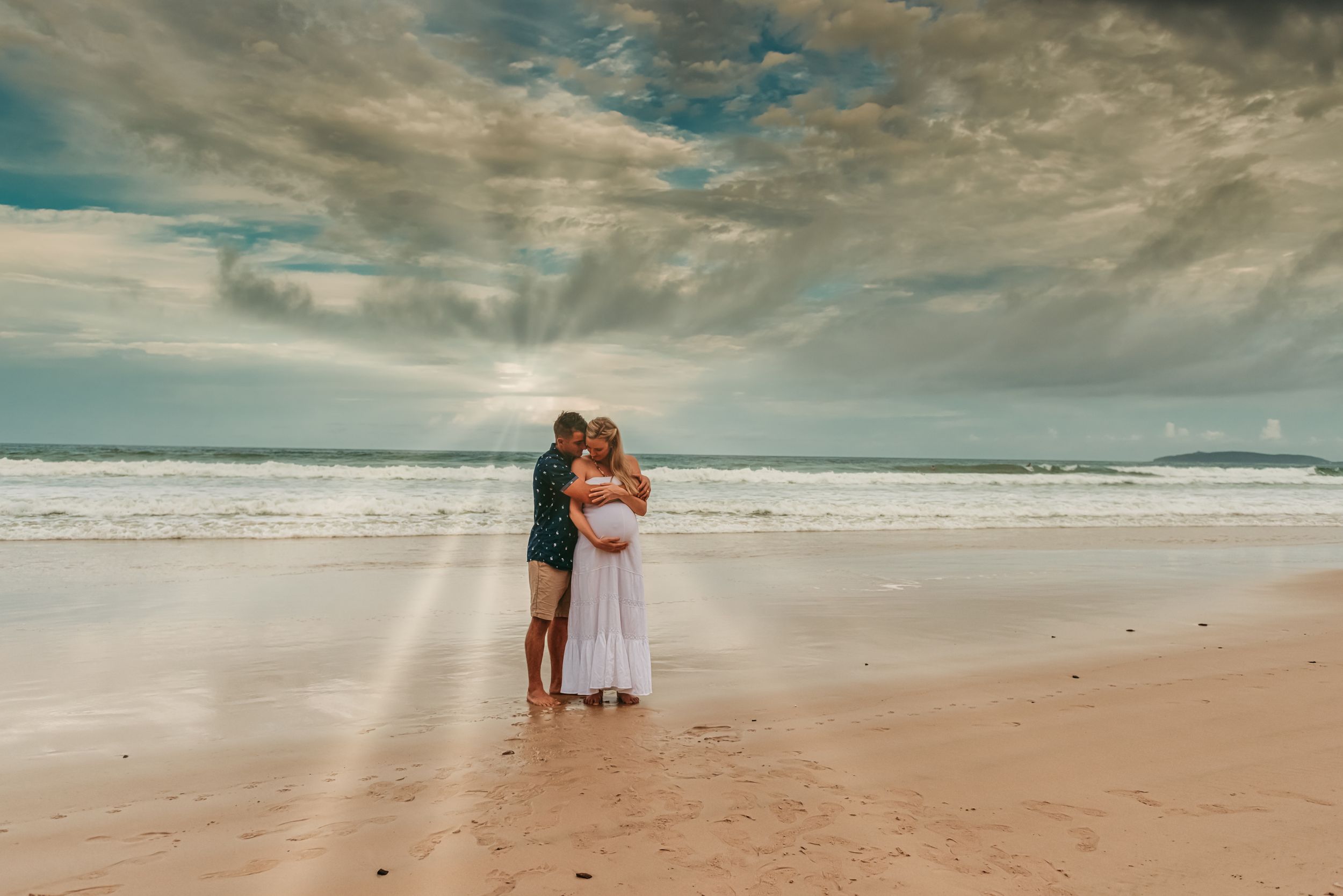 A romantic beach portrait with dramatic clouds and ocean waves in the background.