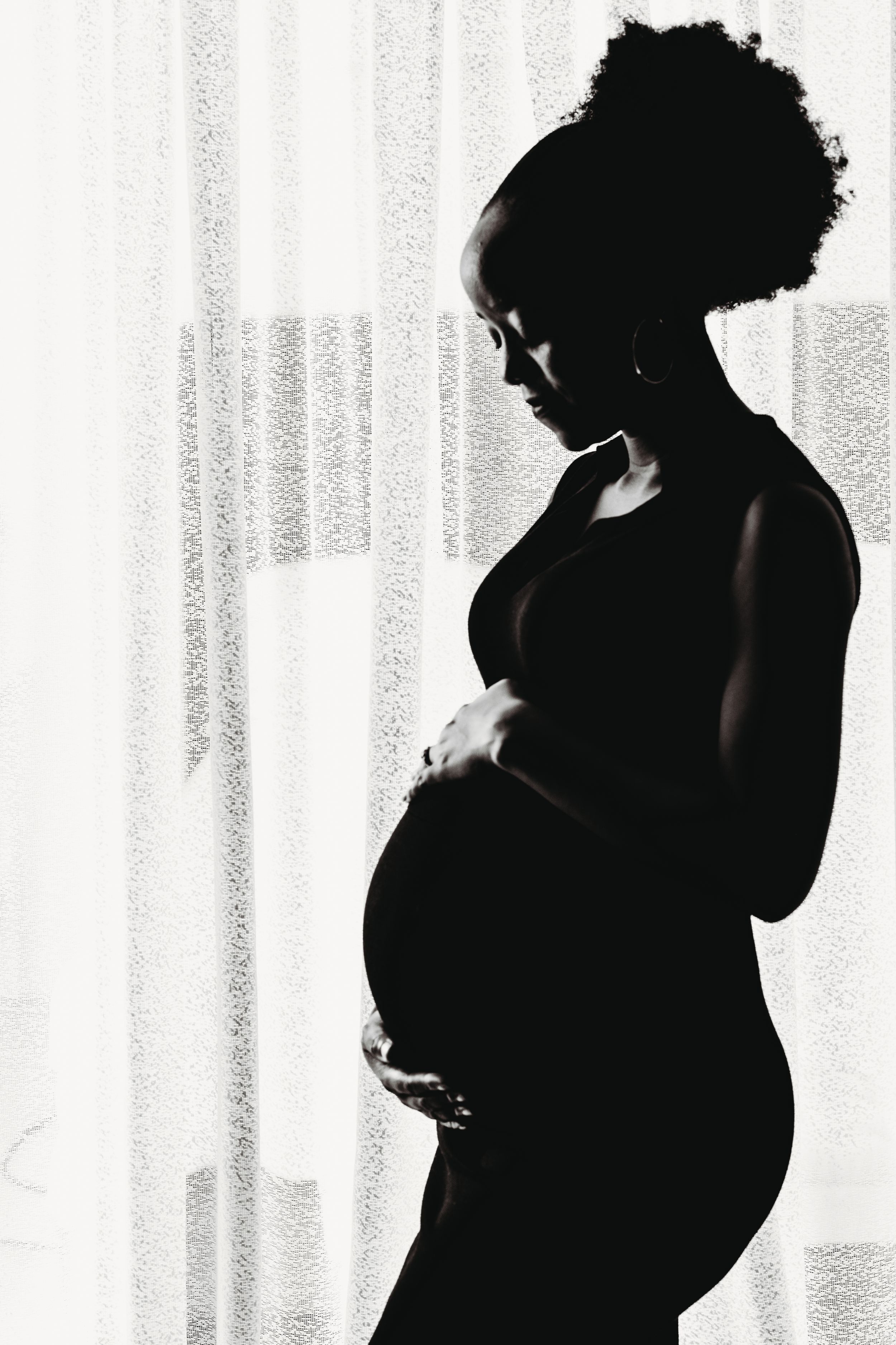 A dramatic silhouette maternity photo of an expectant mother against a light window background.