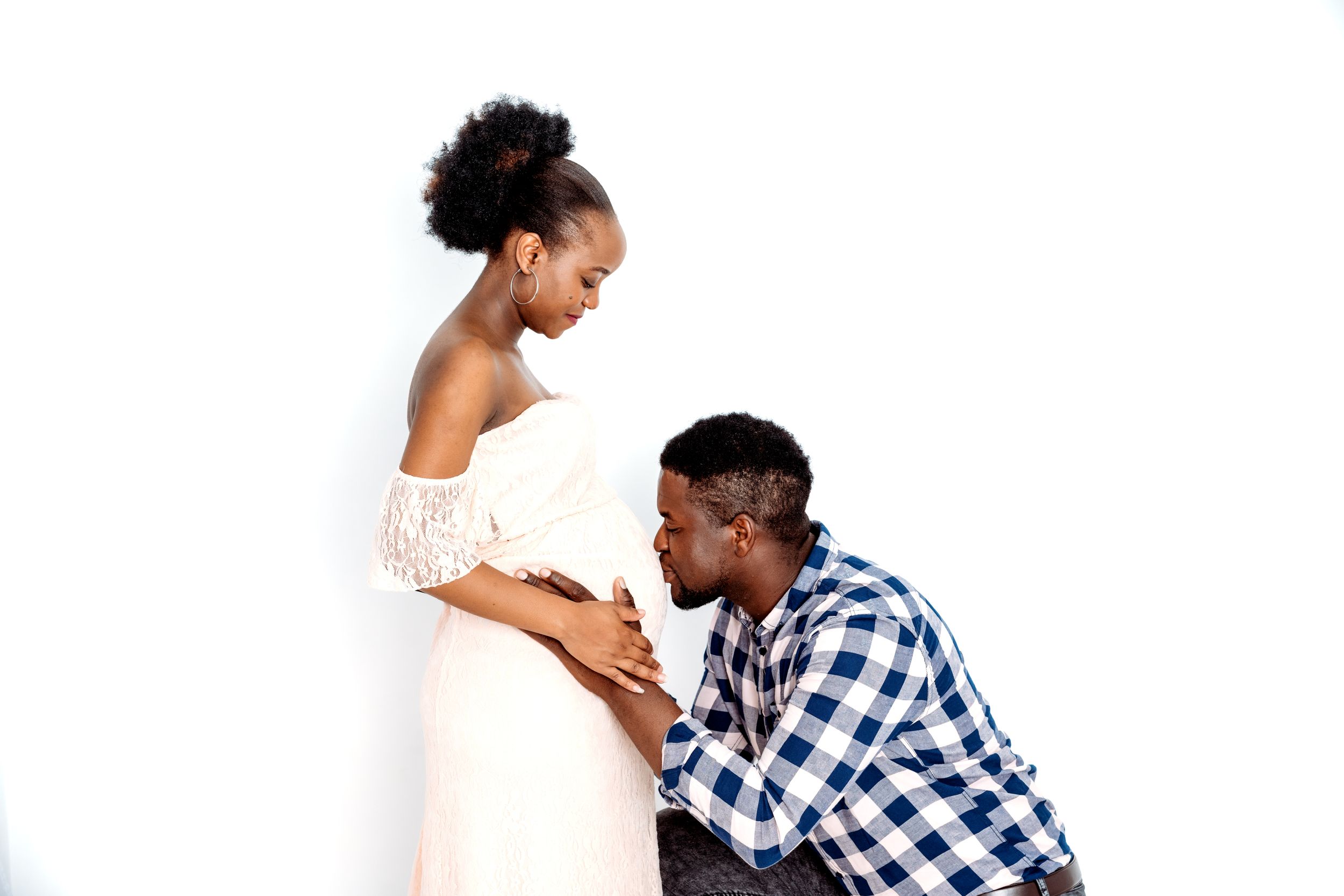 An expectant couple shares an intimate maternity photography moment on a white backdrop.