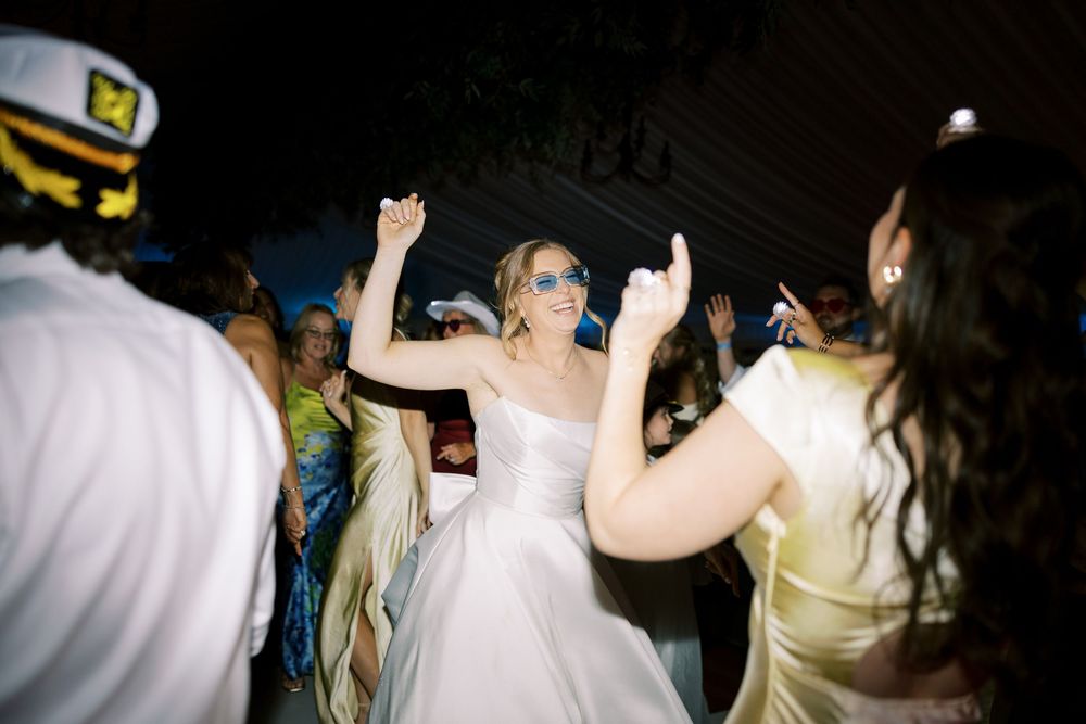 Dancing guests celebrate on a dimly lit dance floor at a wedding reception with a bride in white dress.