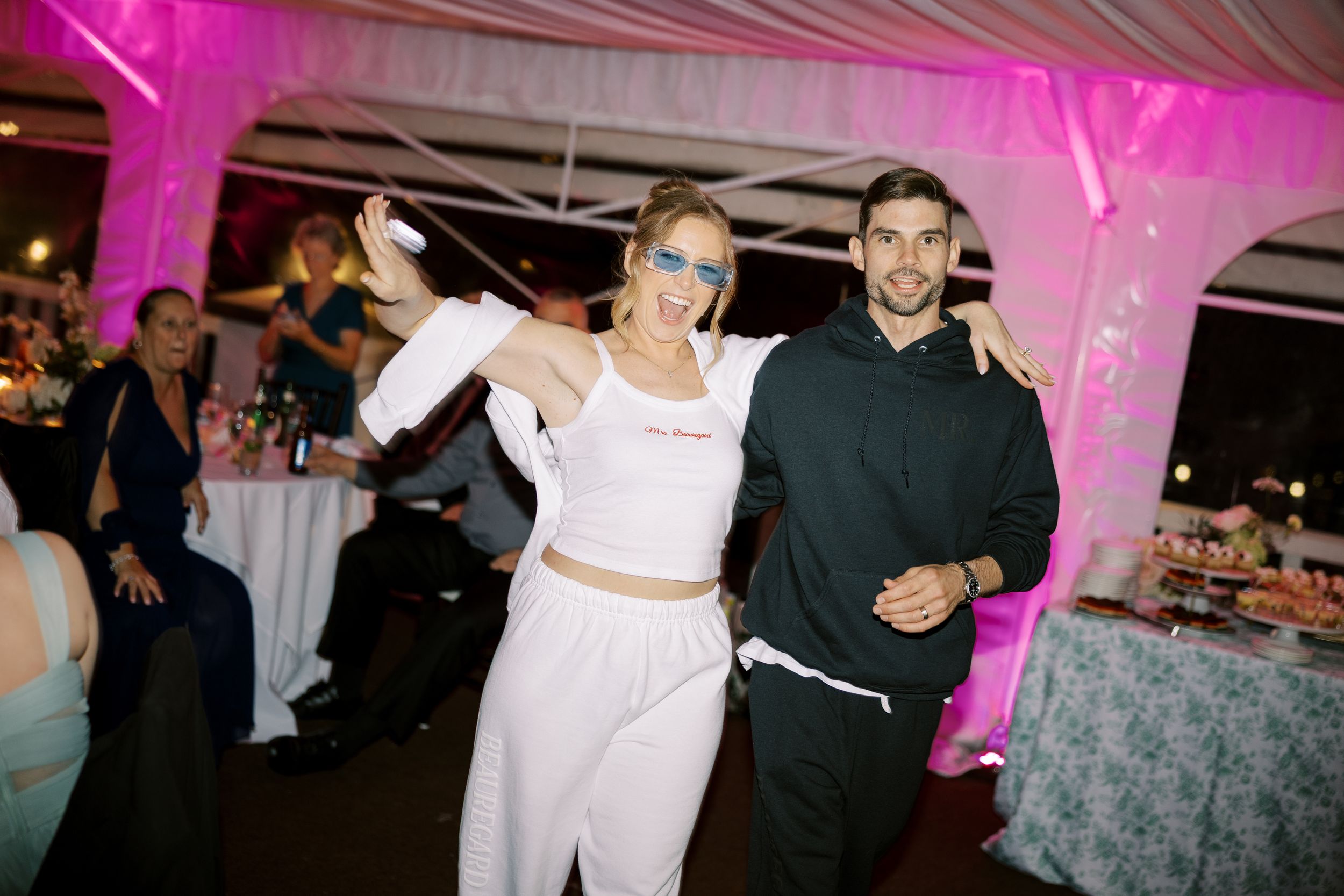 Wedding reception guests enjoying dancing and festivities under pink atmospheric lighting.