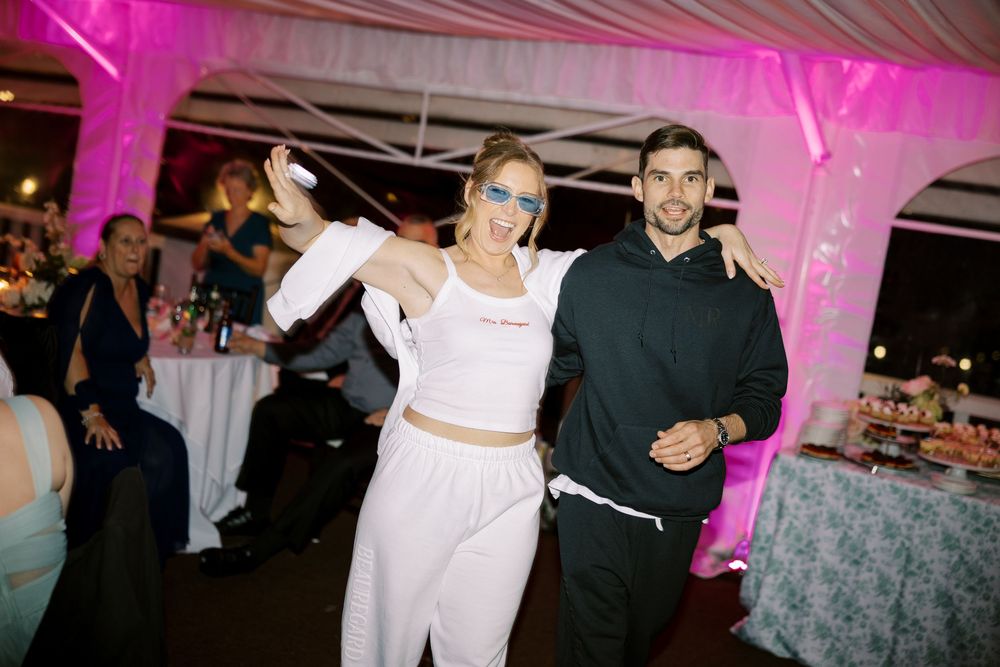 Wedding reception guests enjoying dancing and festivities under pink atmospheric lighting.