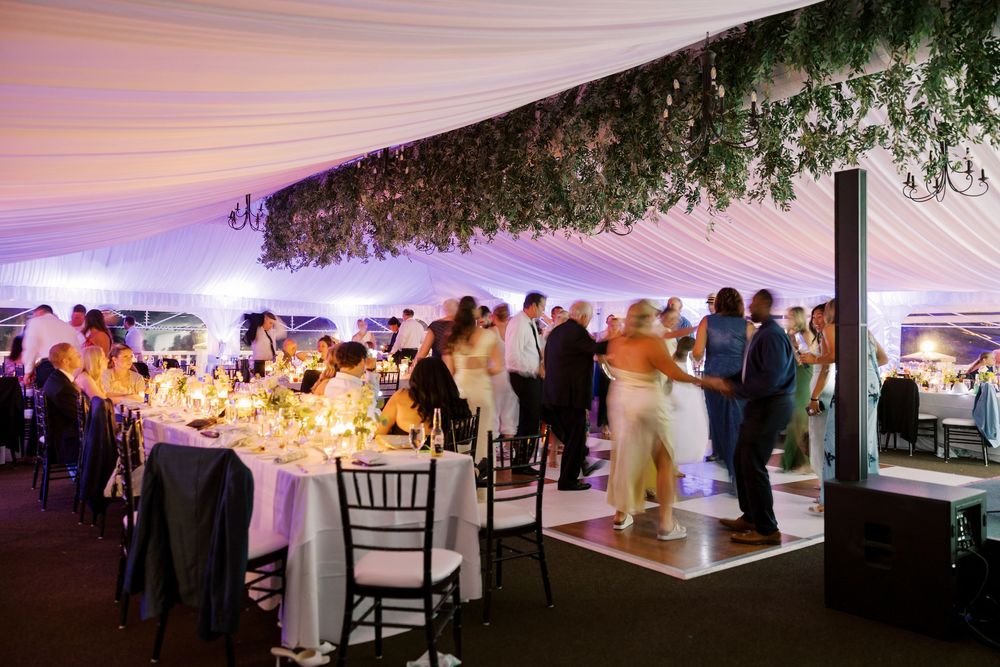 Wedding reception under an elegant white tent illuminated by purple uplighting as guests mingle during the evening celebration.