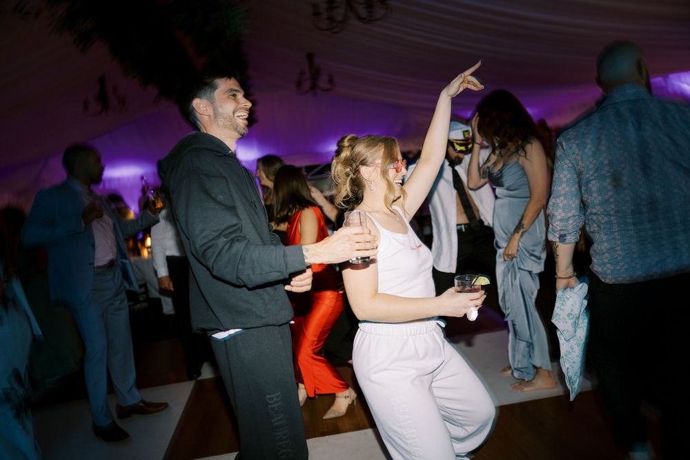 People dance together in purple mood lighting on a dance floor during a social event.