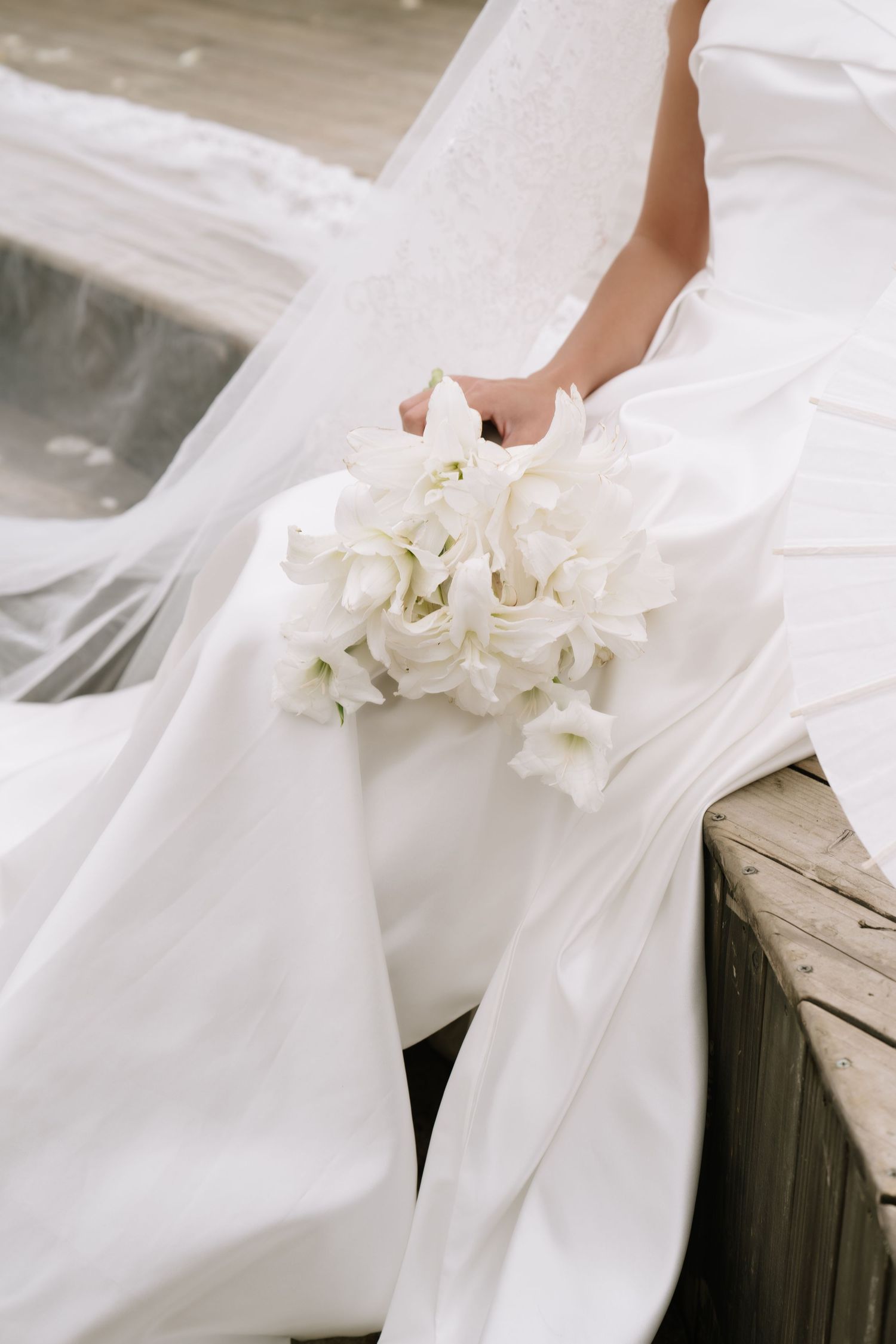 Close-up of bride in white lace wedding dress holding delicate white flower bouquet on wooden steps.