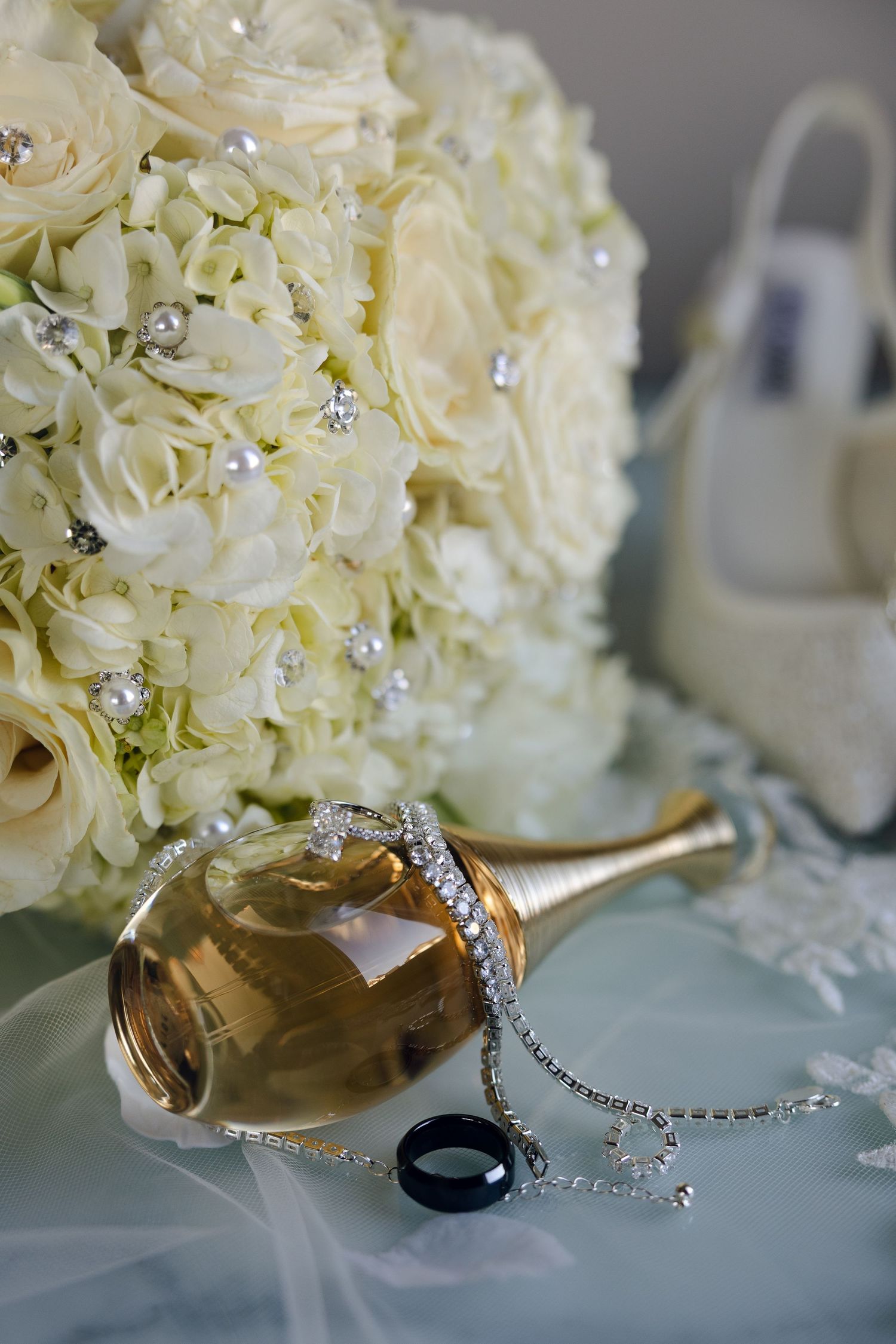 Beautiful white floral wedding bouquet with gold shoes and crystal accessories on soft blue table cloth.