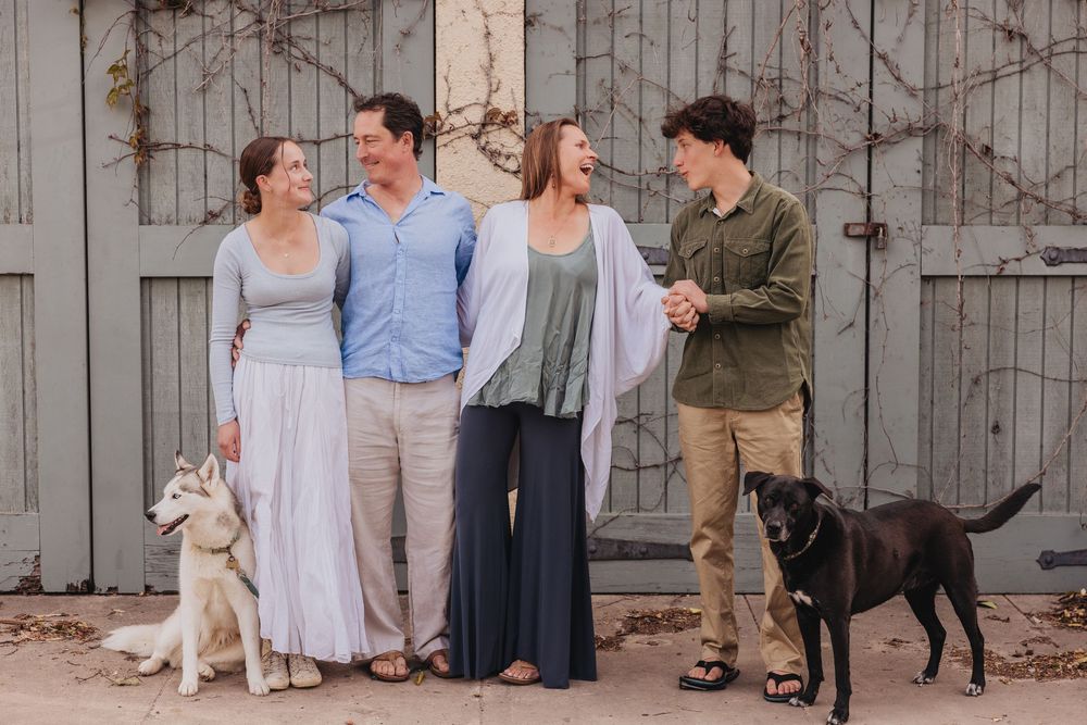 Group of people enjoying a casual outdoor gathering with dogs along a rustic barn wall setting.