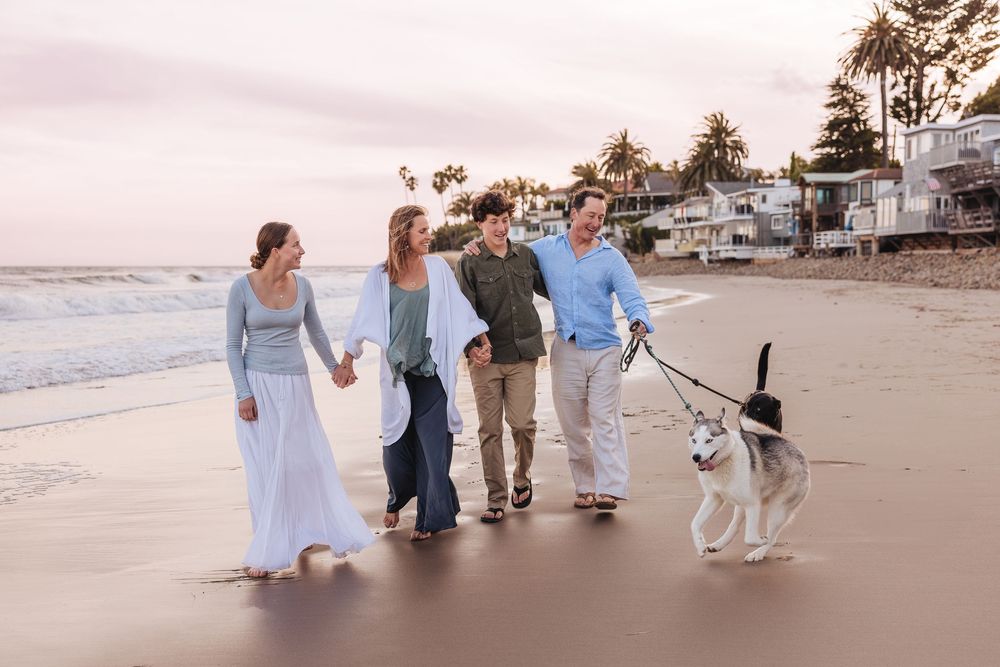 A group walks together along a beach at sunset with their dogs, enjoying the coastal scenery.