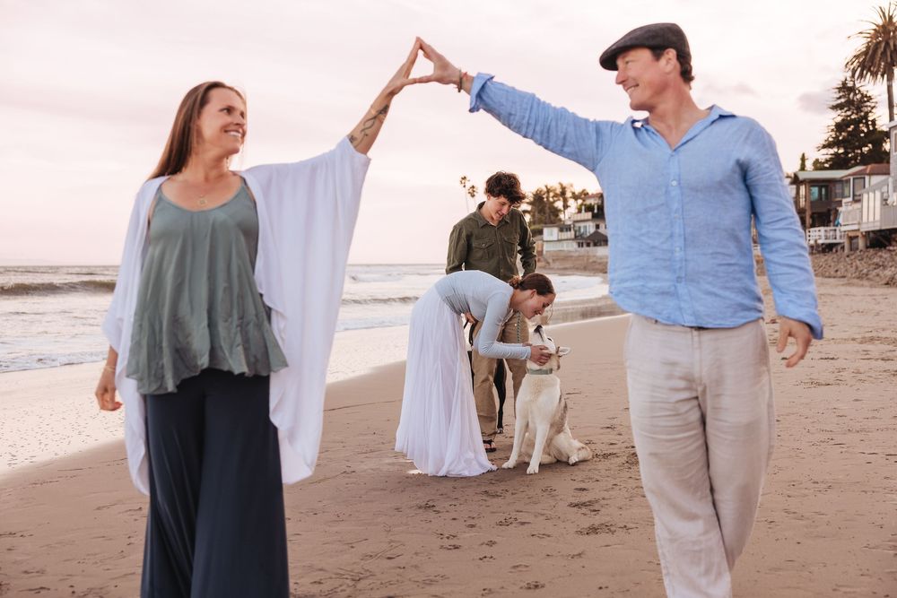 A couple dances playfully on the beach at sunset while others gather in the background.