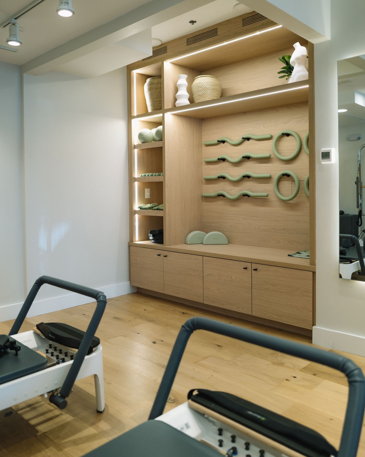 Modern gym facility with mounted wall mirrors, built-in storage cabinets, and hardwood flooring illuminated by recessed lighting.