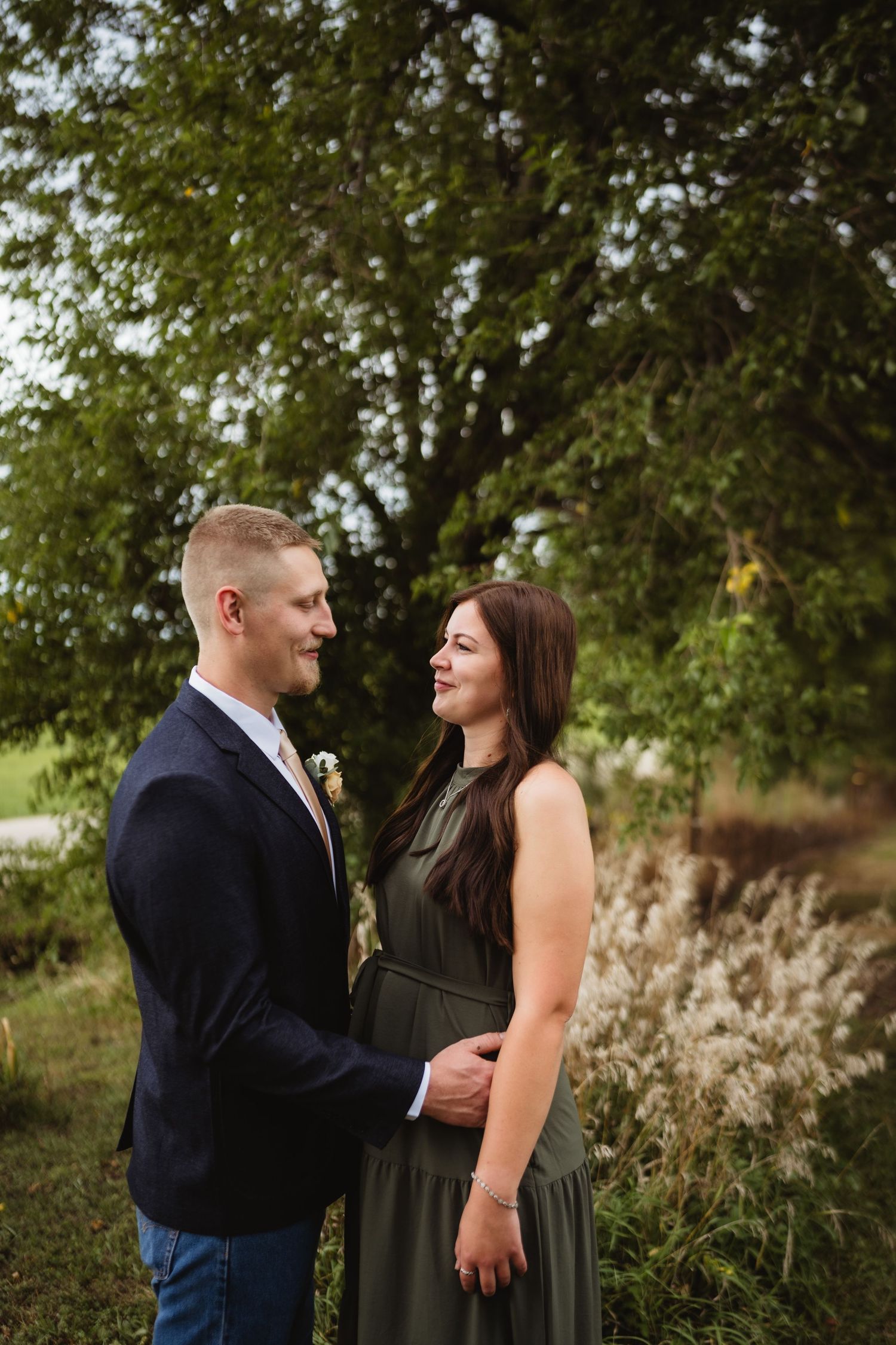 A romantic couple shares tender moments in an outdoor setting with trees and tall grass in the background.