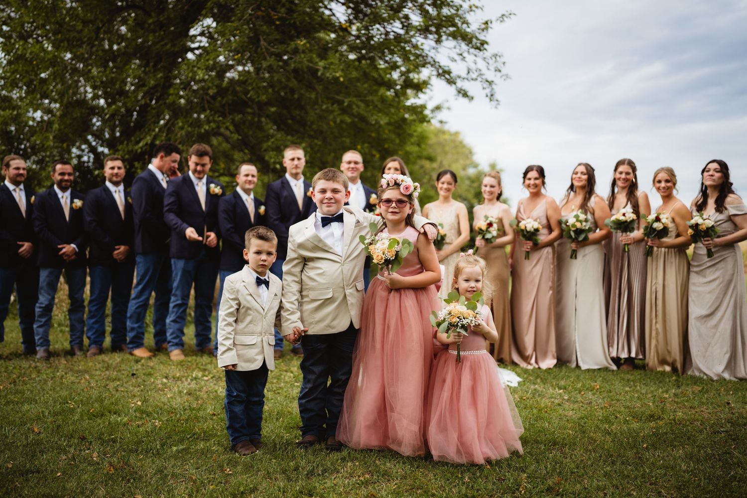 Wedding party members pose together outdoors in neutral tones for a group portrait on a sunny day.