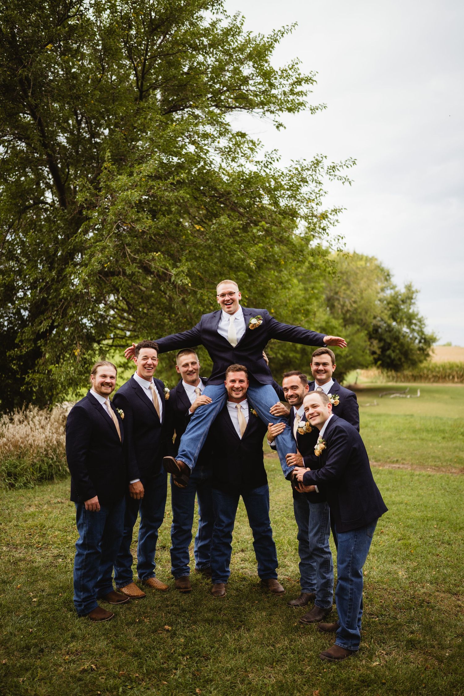 A group in navy suits pose playfully in sequence on grass, showing progressively more energetic and candid interactions.