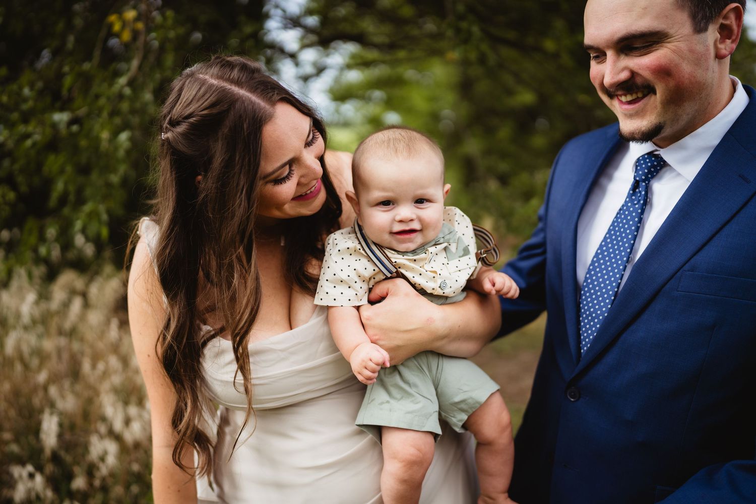 Family wearing blue and white outfits share joyful moments at outdoor photo session in natural setting.
