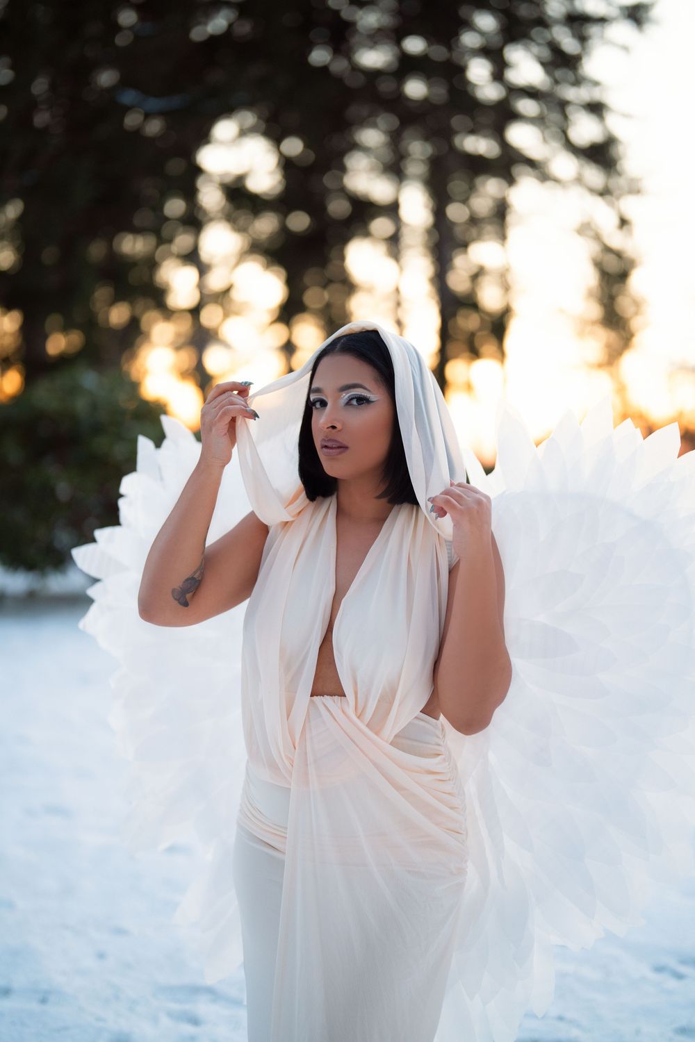 A person in a flowing white dress poses gracefully in a snowy winter landscape during golden hour sunset.