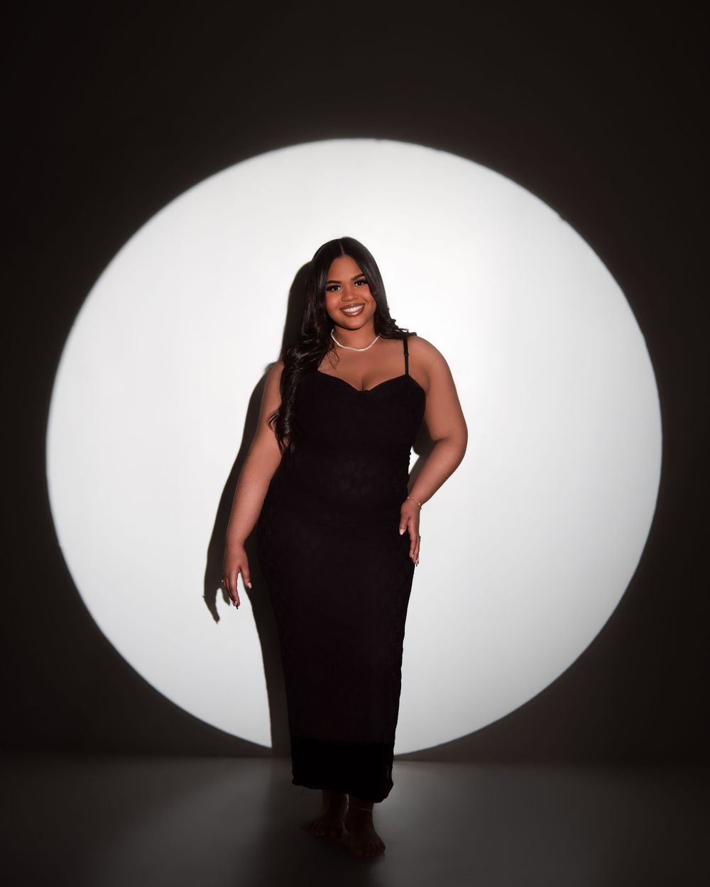 A silhouette figure poses in front of a large oval white light against a dark background in a series of photos.