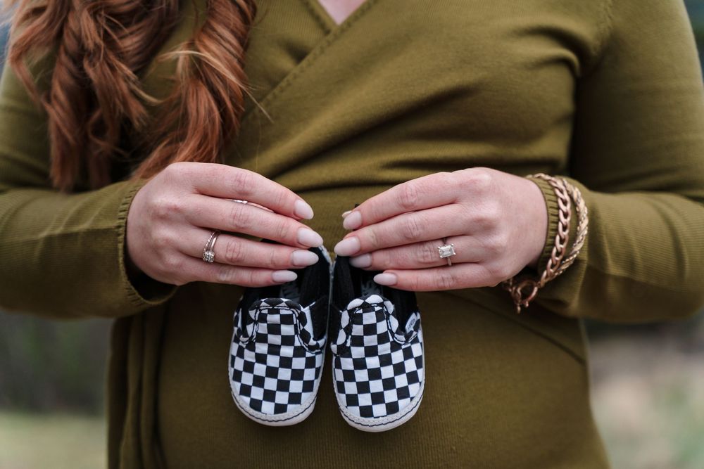 Hands holding small checkered baby shoes against an olive green sweater.