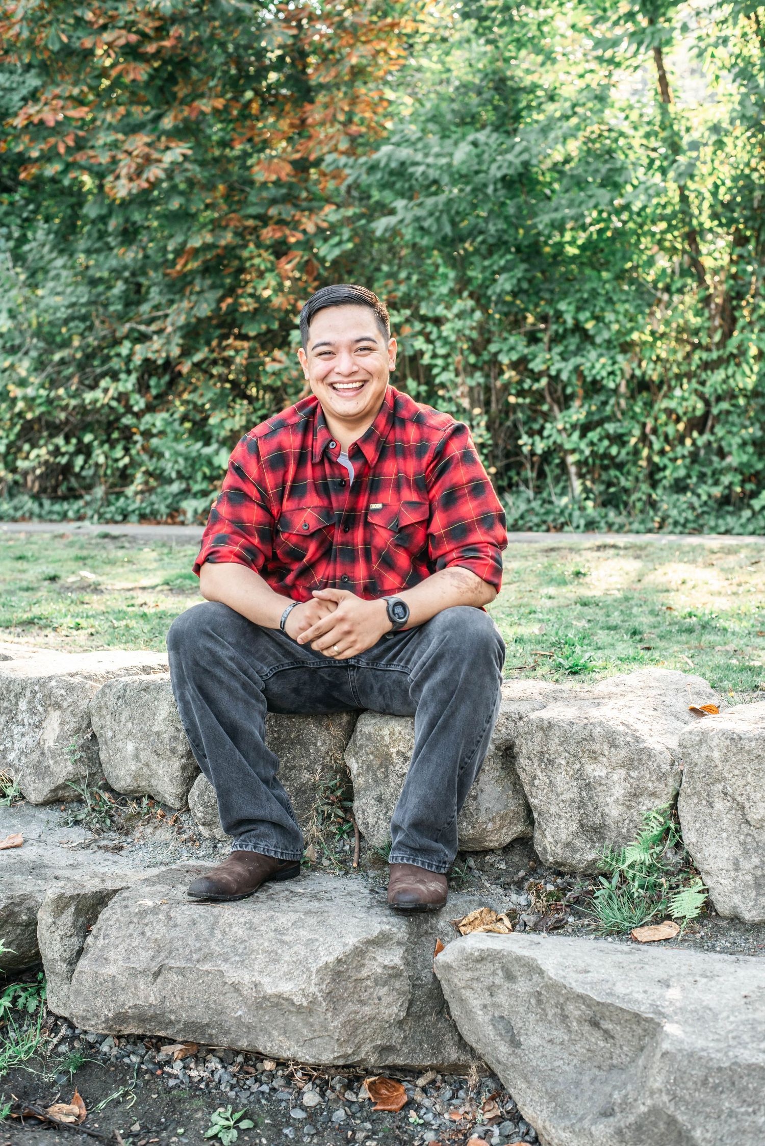 Person in red plaid shirt sitting and smiling on large rocks in natural outdoor setting.