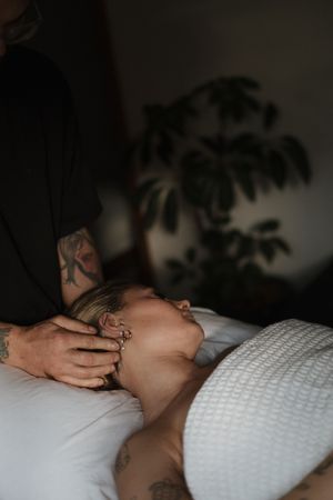 Hands gently caress someone resting on a white textured pillow in a dimly lit room.