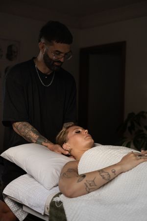 A massage therapist performs a relaxing neck massage on a client laying on a white massage table.
