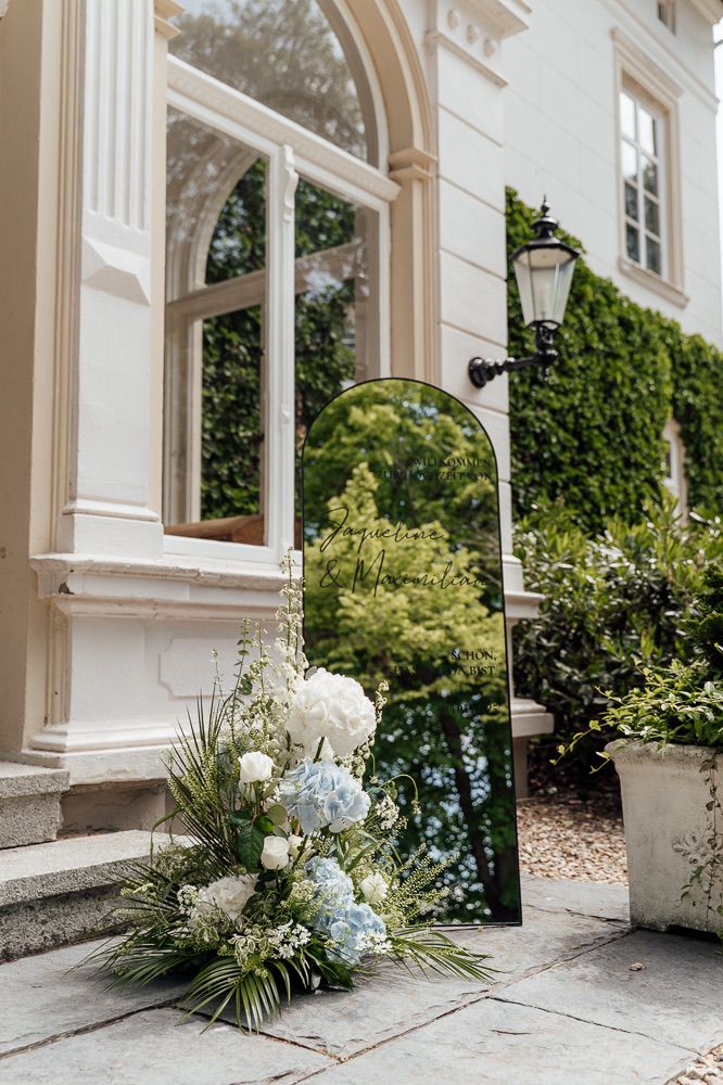 White and blue floral arrangements line the base of elegant white columns along a building's exterior.