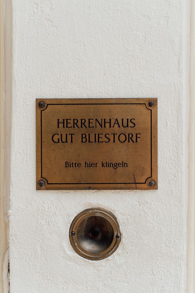 Three brass doorbell plates mounted on a white wall display German text including 'Herrenhaus' and 'Gut Bliestorf'.