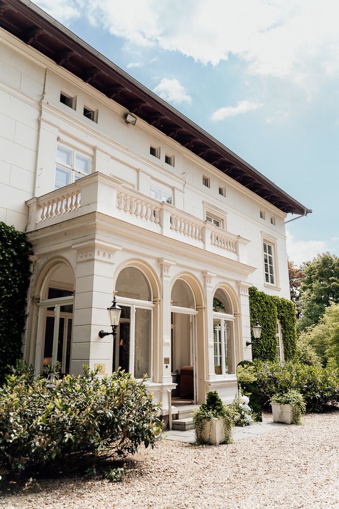 Elegant white Mediterranean-style villa with arched portico and landscaped gravel driveway showcases classic architectural details.