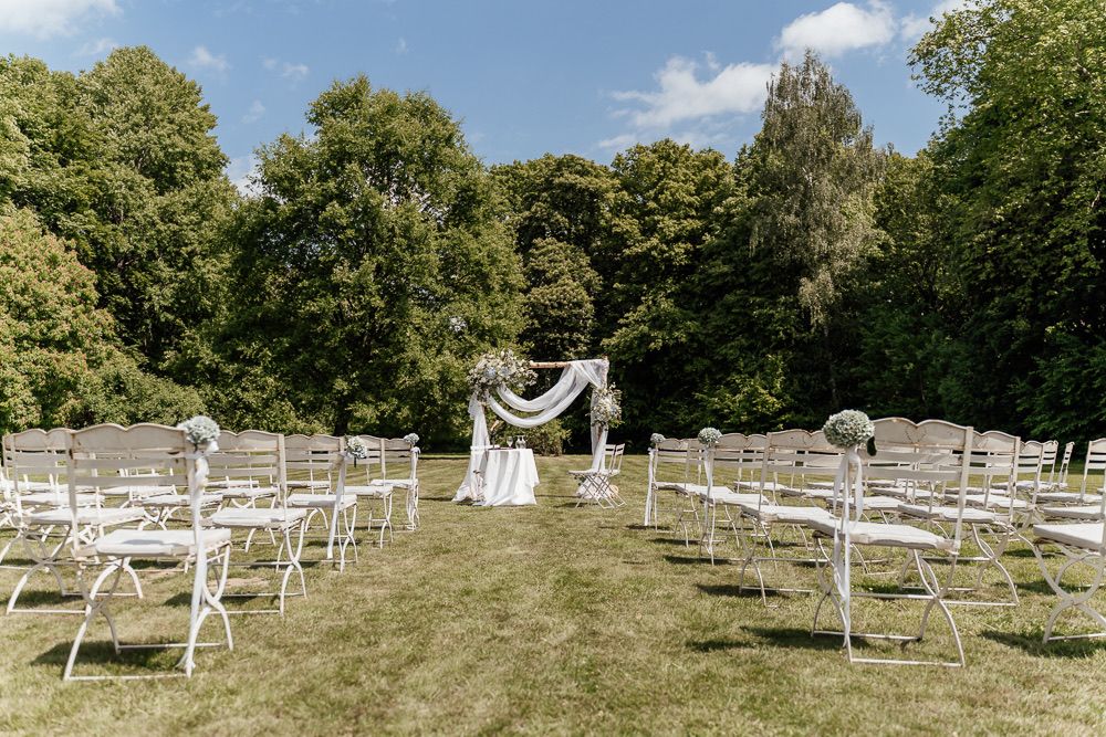 White wooden benches arranged in rows on a grassy hillside under blue sky and trees.