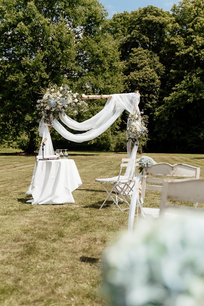 Wedding ceremony arch with flowing white fabric and floral decor set up on green lawn.