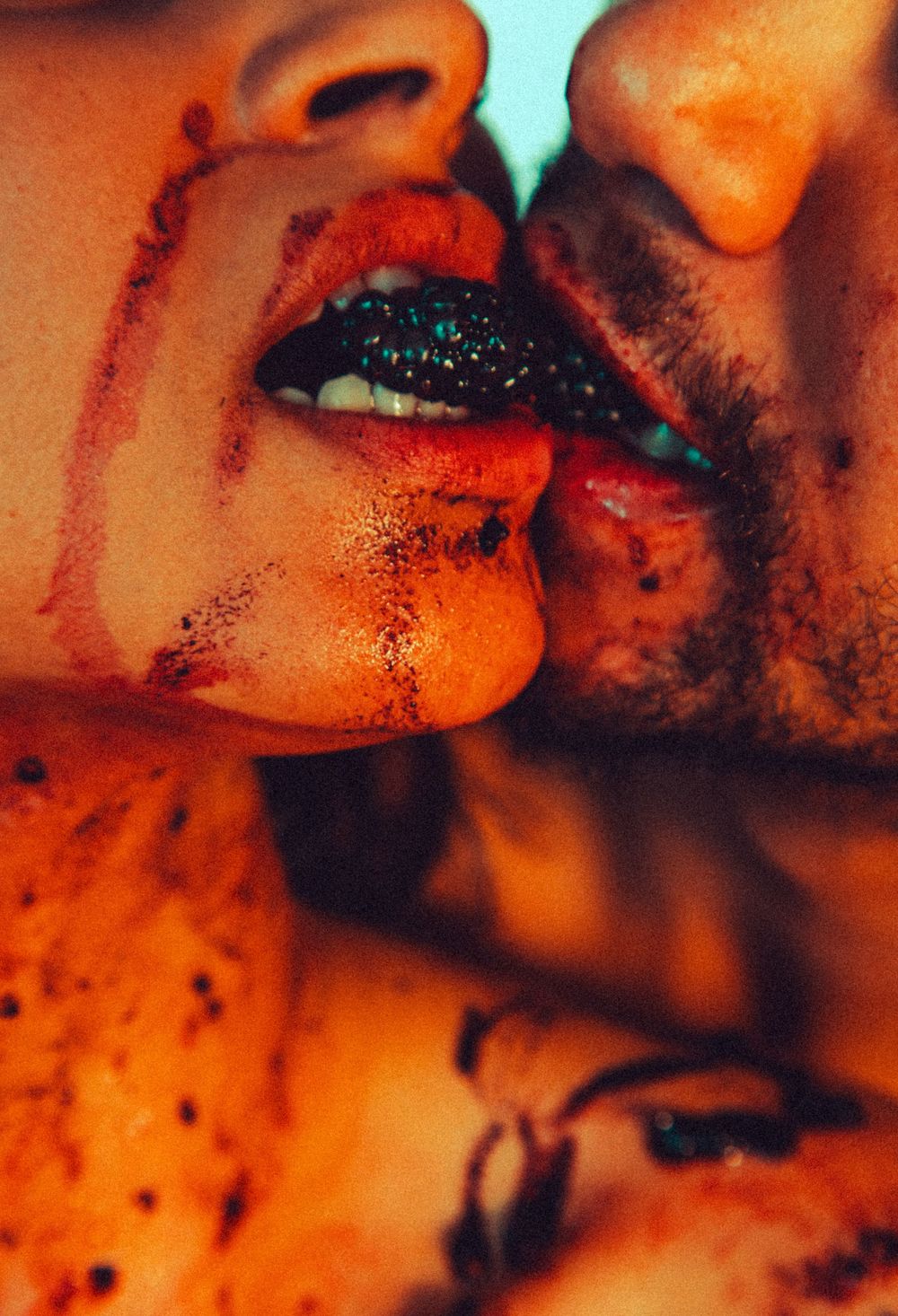 Close-up of two people sharing an intimate kiss with dark glittery lips and scattered speckles on skin.
