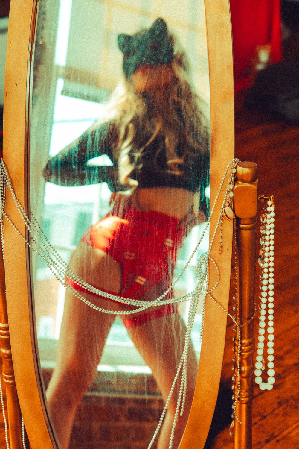 Woman in red shorts reflected in ornate mirror decorated with pearl bead chains.
