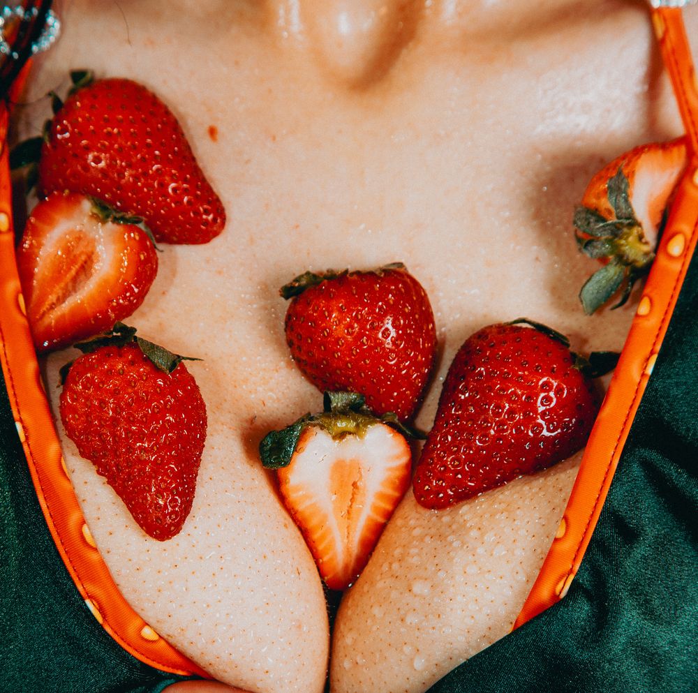 Fresh sliced and whole strawberries arranged on a person's chest wearing an orange and green bikini top.