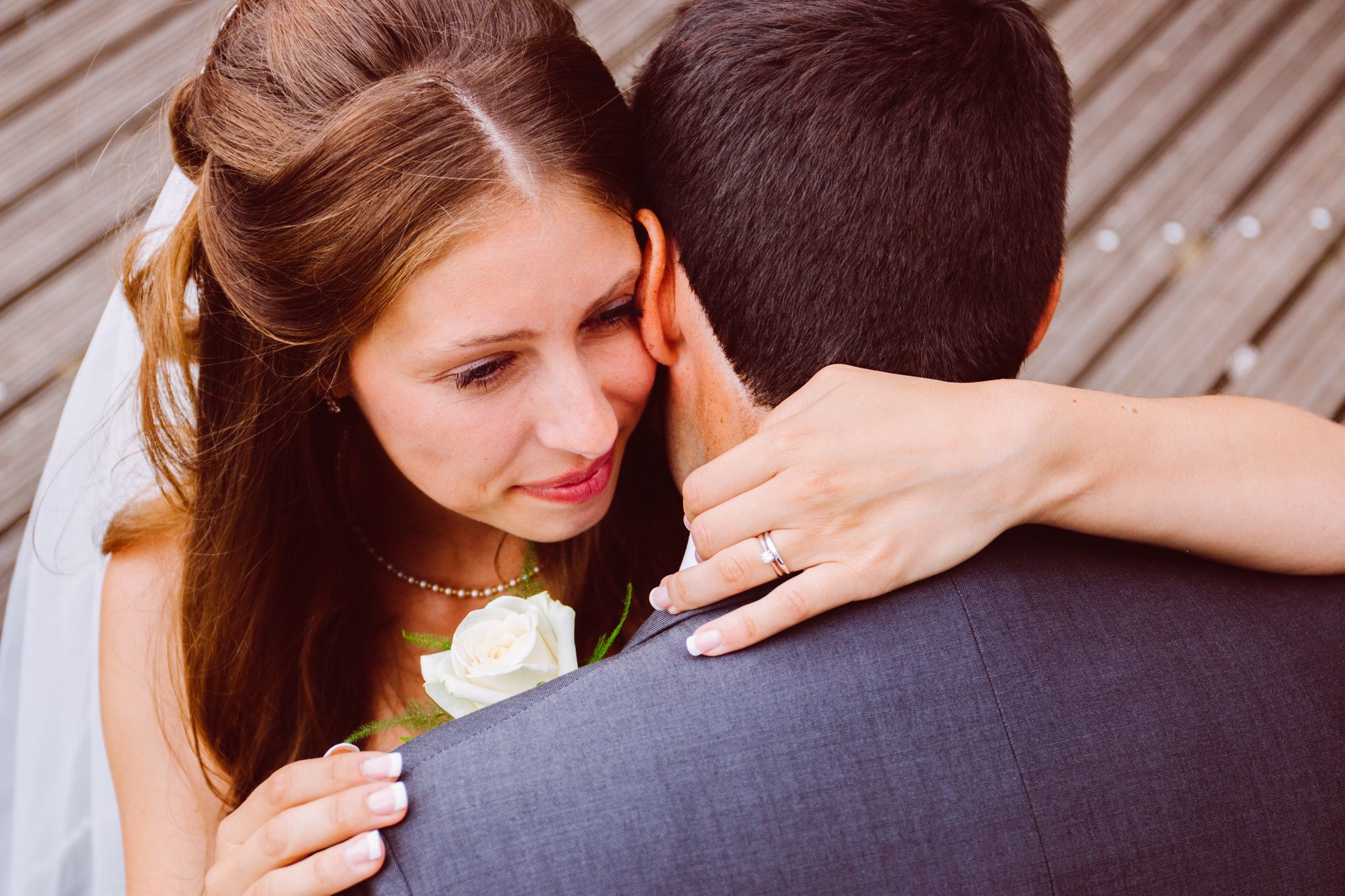 Close-up view of a couple embracing, with white rose boutonniere visible on dark suit jacket.