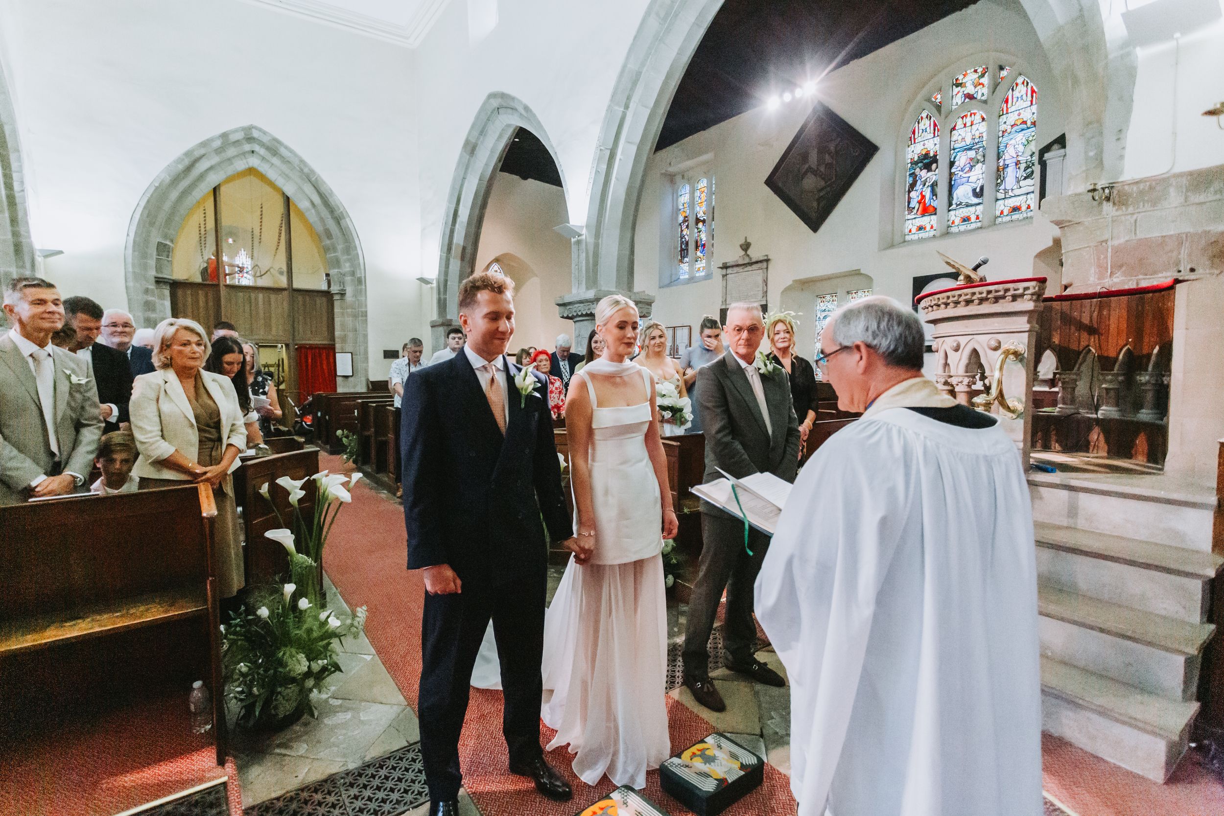Couple exchanging vows at a traditional church wedding ceremony, standing before an officiant in white robes.