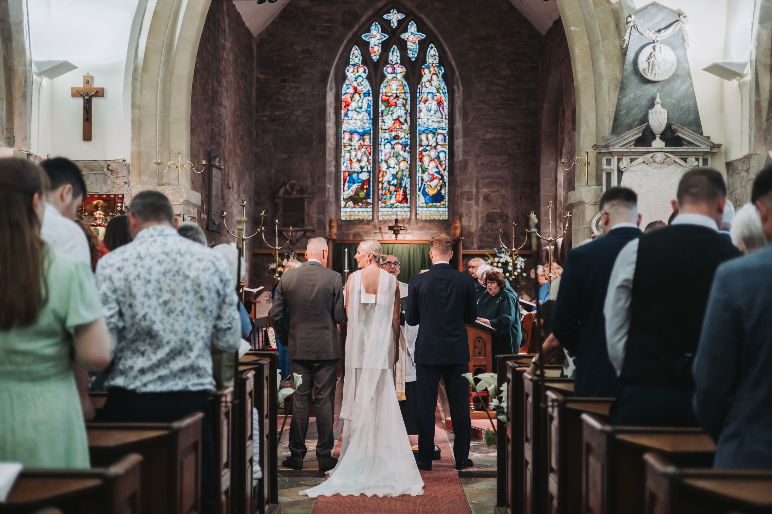 Bride and groom walking down the aisle of a traditional stone church with stained glass windows during wedding ceremony.