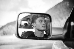 Black and white photos of senior boy sitting in his truck looking out his side view mirror reflection.