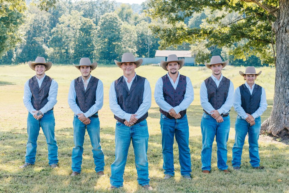 Groomsmen in matching blue jeans and vests pose together outdoors.