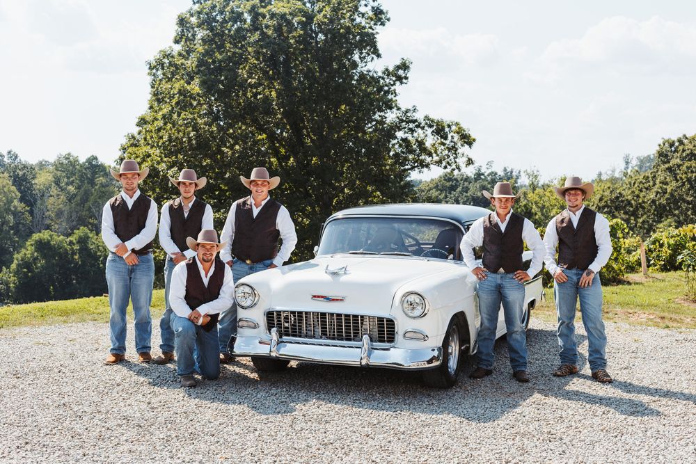 Wedding party members in casual western wear gather around a vintage white automobile.