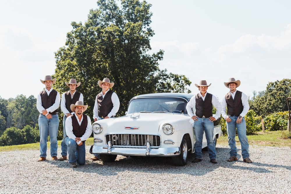 Groomsmen in western attire pose with a classic white car outdoors.
